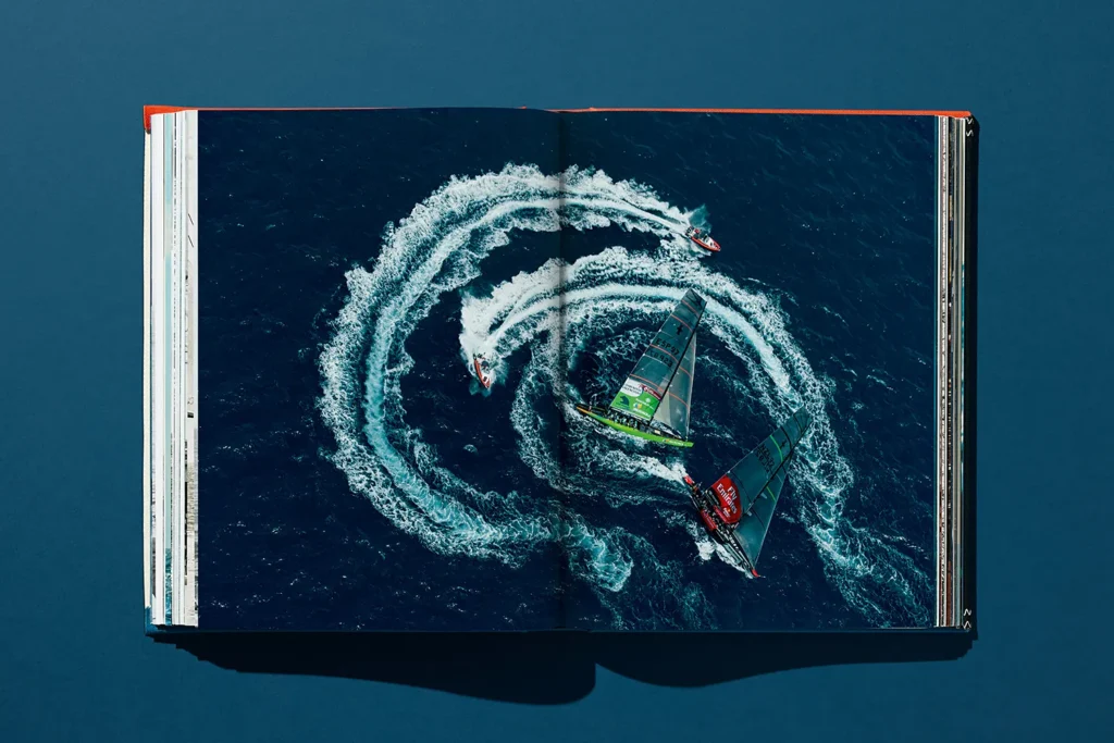 Aerial view of two high-tech America’s Cup racing yachts encircled by motorboats creating water trails