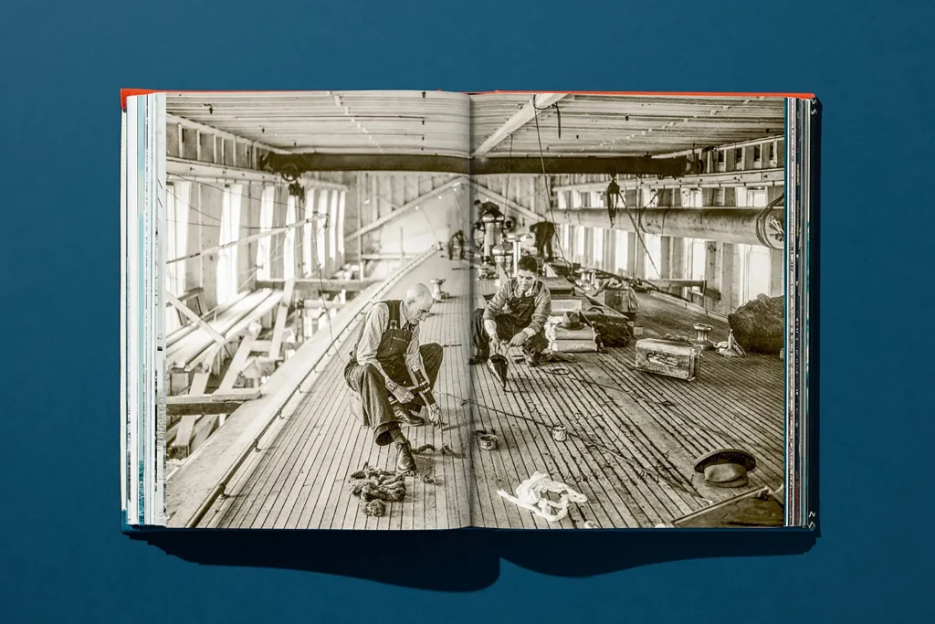 Black and white archival photo of craftsmen working on the wooden deck of a yacht inside a shipyard